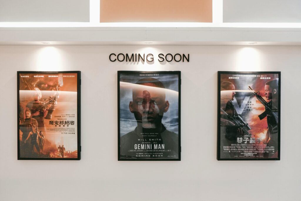 Framed posters of upcoming movies in a cinema hallway under 'Coming Soon' sign.